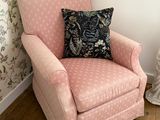 une chaise rose avec un coussin posé dessus, dans un coin de la pièce
