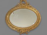 an oval mirror with a gold frame on a gray wall