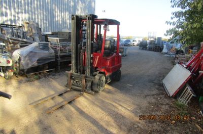 un chariot élévateur rouge garé à côté d'un tas de ferraille
