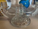 a glass candle holder on a table with a blue vase in the background