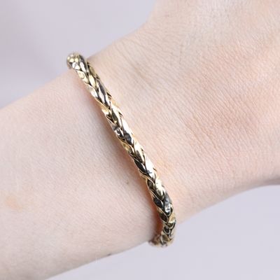 the woman is wearing a gold bracelet that has a braid design on it