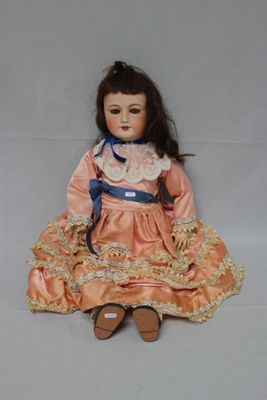 an antique doll sitting on a white surface wearing a pink dress and blue ribbon