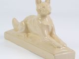 beige ceramic sculpture of a dog laying down on a wooden base