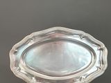 une assiette en argent posée sur un socle en bois, sur fond gris