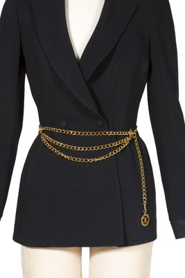 un gros plan sur le torse d'un mannequin portant un blazer noir et une ceinture à chaîne dorée