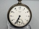 a silver pocket watch with a white face on a clear stand