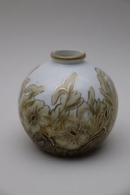 un vase blanc et doré posé sur une surface blanche