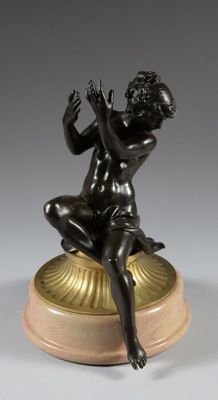 une figurine antique en bronze représentant un garçon assis sur un coquillage