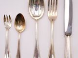 five silver spoons, a knife, and a fork on a white surface
