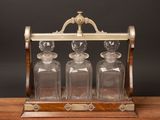an old fashioned glass decanter with three glass bottles on a wooden stand