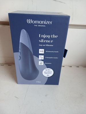 emballage d'un appareil « Womanizer » posé sur un comptoir devant un mur blanc