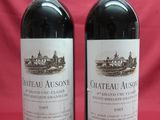 two bottles of red wine sitting on top of a red cloth