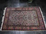 a rug on the floor with a vase of flowers in the background