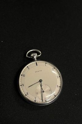 a silver pocket watch sitting on a black surface
