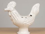 a white ceramic rooster on a table with a gray background