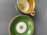 pair of green and gold cups and saucers on a gray surface