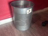 a metal trash can sitting on the floor next to a red wall