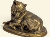 statue en bronze représentant un chien couché sur un plateau, sur fond blanc