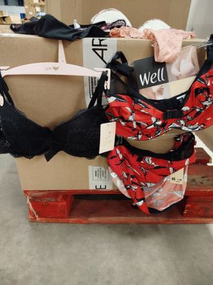 Des cartons contenant des soutiens-gorge et des sous-vêtements sont empilés sur une palette dans un entrepôt