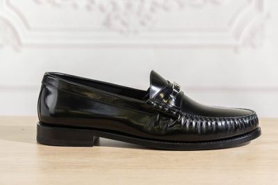 a close up of a black loafer on a wooden table