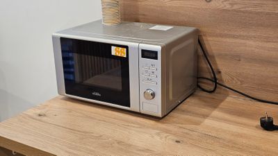a microwave sitting on a wooden table with a cup on top of it