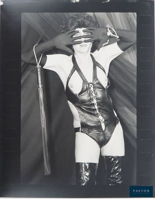 photographie en noir et blanc d'une femme vêtue d'une tenue en latex et tenant un fouet