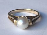 ring with a pearl in the middle of it on a white surface