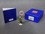 une petite figurine représentant un homme en costume vert, à côté d'une boîte bleue
