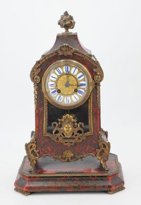 a red and gold clock sitting on a white surface