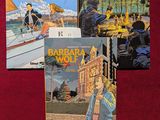 trois livres posés sur un tissu rouge orné de l'image d'une femme sur un bateau