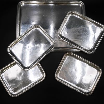 quatre plateaux en argent avec couvercles, posés sur une surface noire