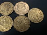 five gold sovereigns of different sizes and shapes on a black surface