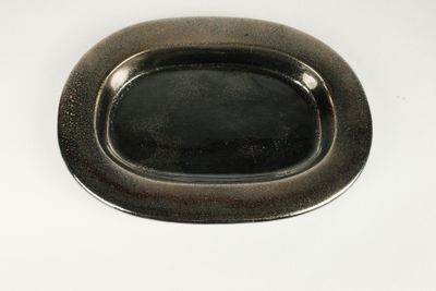 une assiette noire posée sur une table blanche, avec une poignée en argent