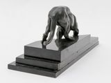 statue of a man bending over on a platform with his foot on the ground