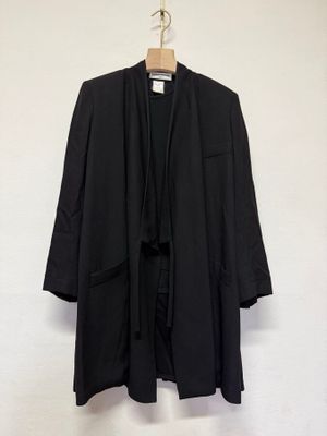 une veste noire suspendue à un cintre devant un mur blanc