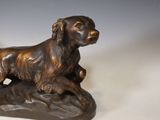 bronze statue of a dog sitting on a rock on a white surface