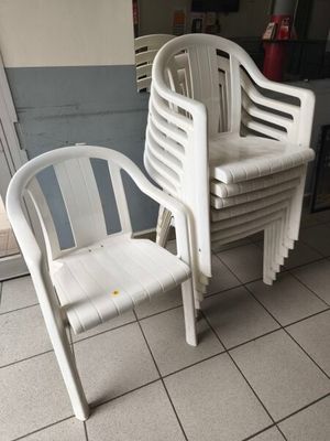 plusieurs chaises en plastique blanc posées sur un sol carrelé à côté d'une porte