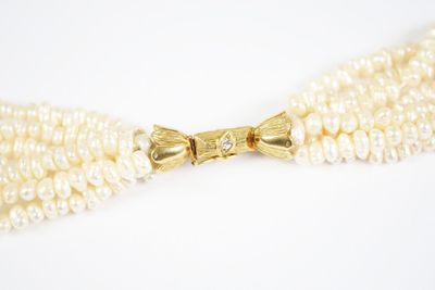 a close up of a white pearl necklace with a gold bow