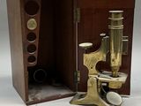 un microscope ancien en laiton, dans un coffret en bois, posé sur une surface blanche