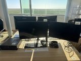 three computer monitors sitting on a desk in front of a window