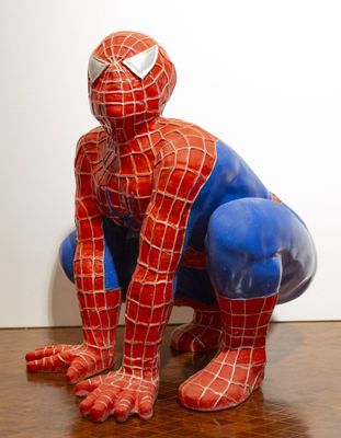 une statue représentant Spider-Man assis sur un plancher en bois