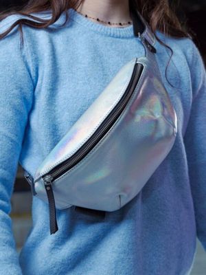 La femme porte un pull bleu et un sac banane argenté.