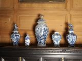 Plusieurs vases bleus et blancs sont posés sur une étagère devant un tableau