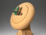 an image of a ring with a green stone on top of a wooden stand