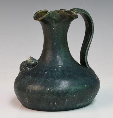 un vase vert muni d'une anse, posé sur une surface blanche