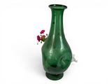 a green vase with a flower in it on a white surface