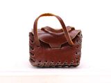 un petit sac à main marron muni d'une anse, posé sur une surface blanche