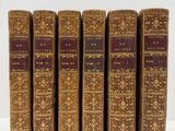six vieux livres sont alignés sur une surface blanche