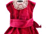 La robe est rouge et comporte un col en dentelle au niveau du cou.