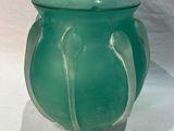 a green glass vase with a curved handle on a white surface